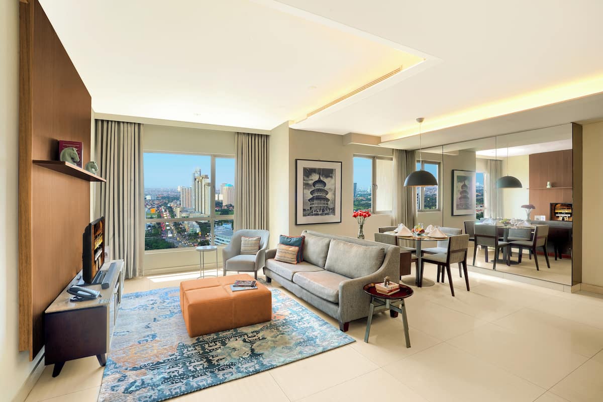 A modern living room with a sofa, ottoman, and coffee table, a dining area with chairs and a table, and a large window with a city view.