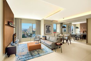 Uma sala de estar moderna com um sofá, um banquinho e uma mesa de centro, uma área de jantar com cadeiras e uma mesa, e uma janela grande com vista para a cidade.