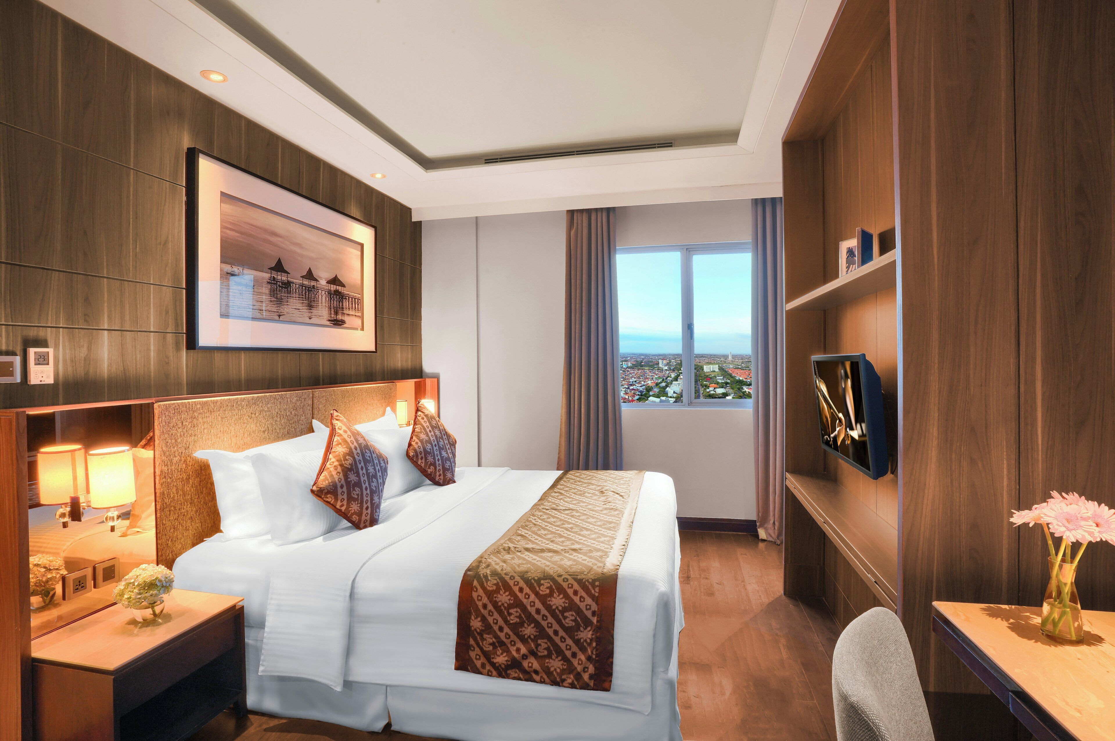 Une chambre d’hôtel avec un grand lit, des lampes de chevet, un téléviseur fixé au mur et une fenêtre donnant sur un beau paysage.