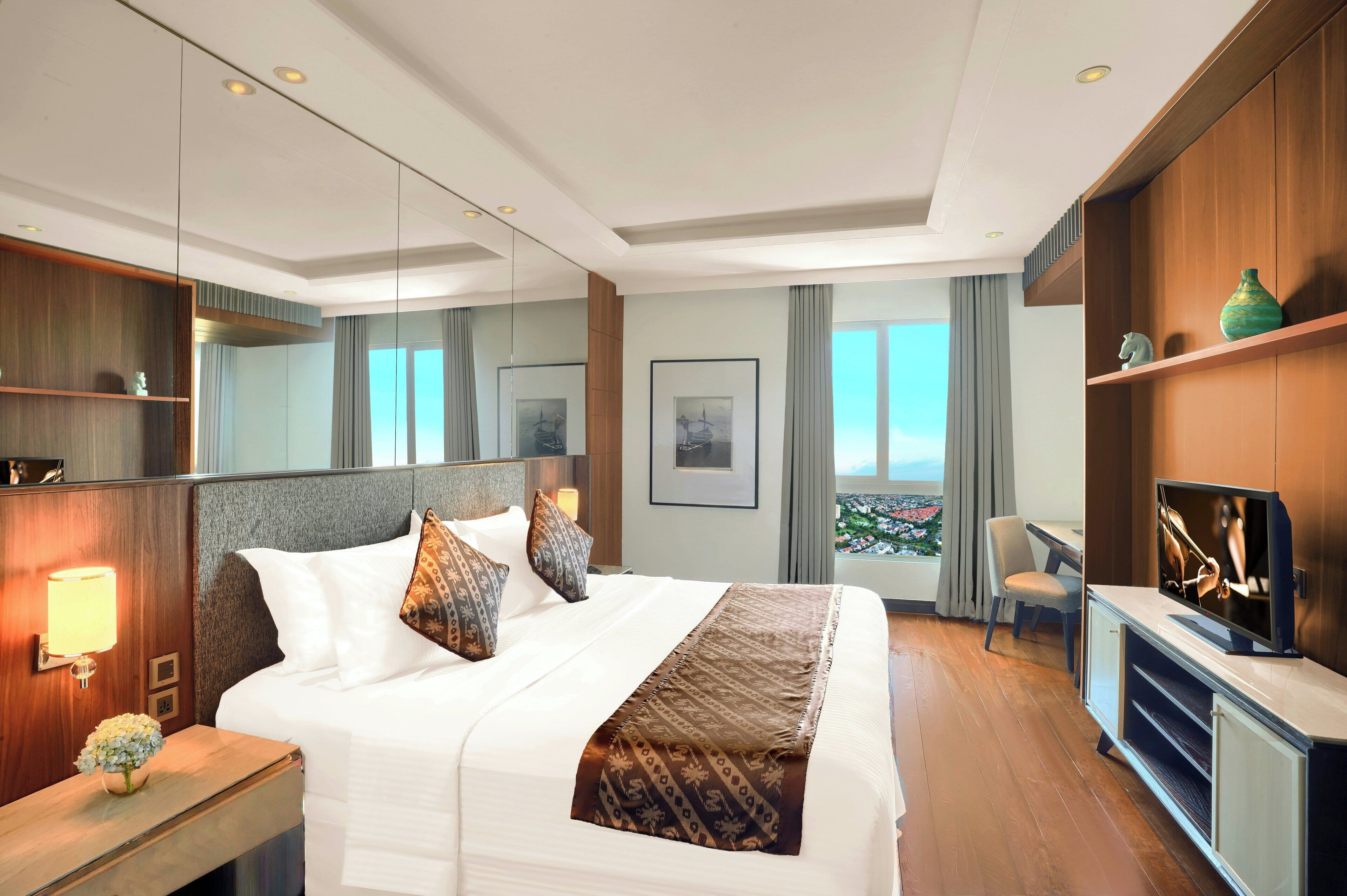 Habitación de hotel con una cama grande, escritorio, televisión y vista a la ciudad.