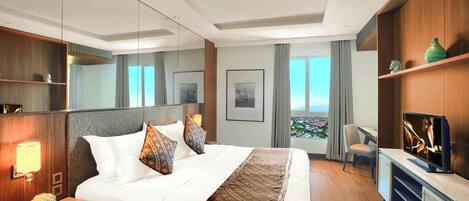 Habitación de hotel con una cama grande, escritorio, televisión y vista a la ciudad.