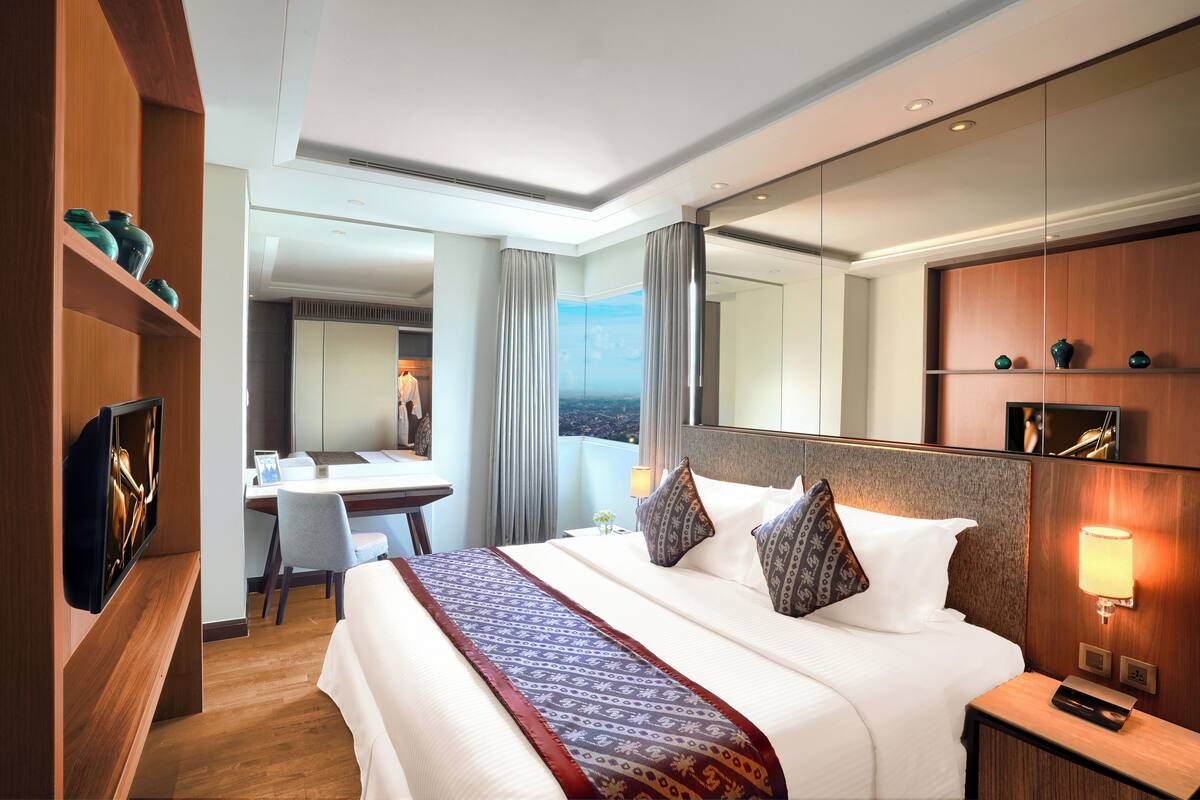 A hotel room with a large bed, a desk, a television, and a view of the city.