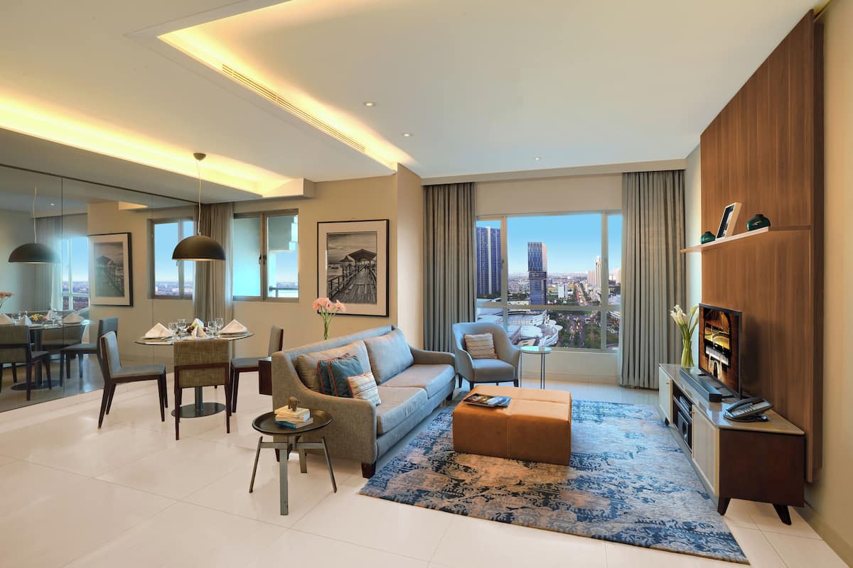 A modern living room with a sofa, armchair, coffee table, TV, and a dining area with a table and chairs.