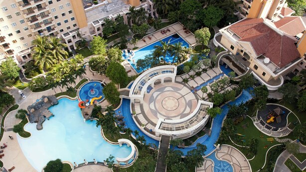 Vista aérea de un resort con varias piscinas, palmeras y una fuente circular en el centro.