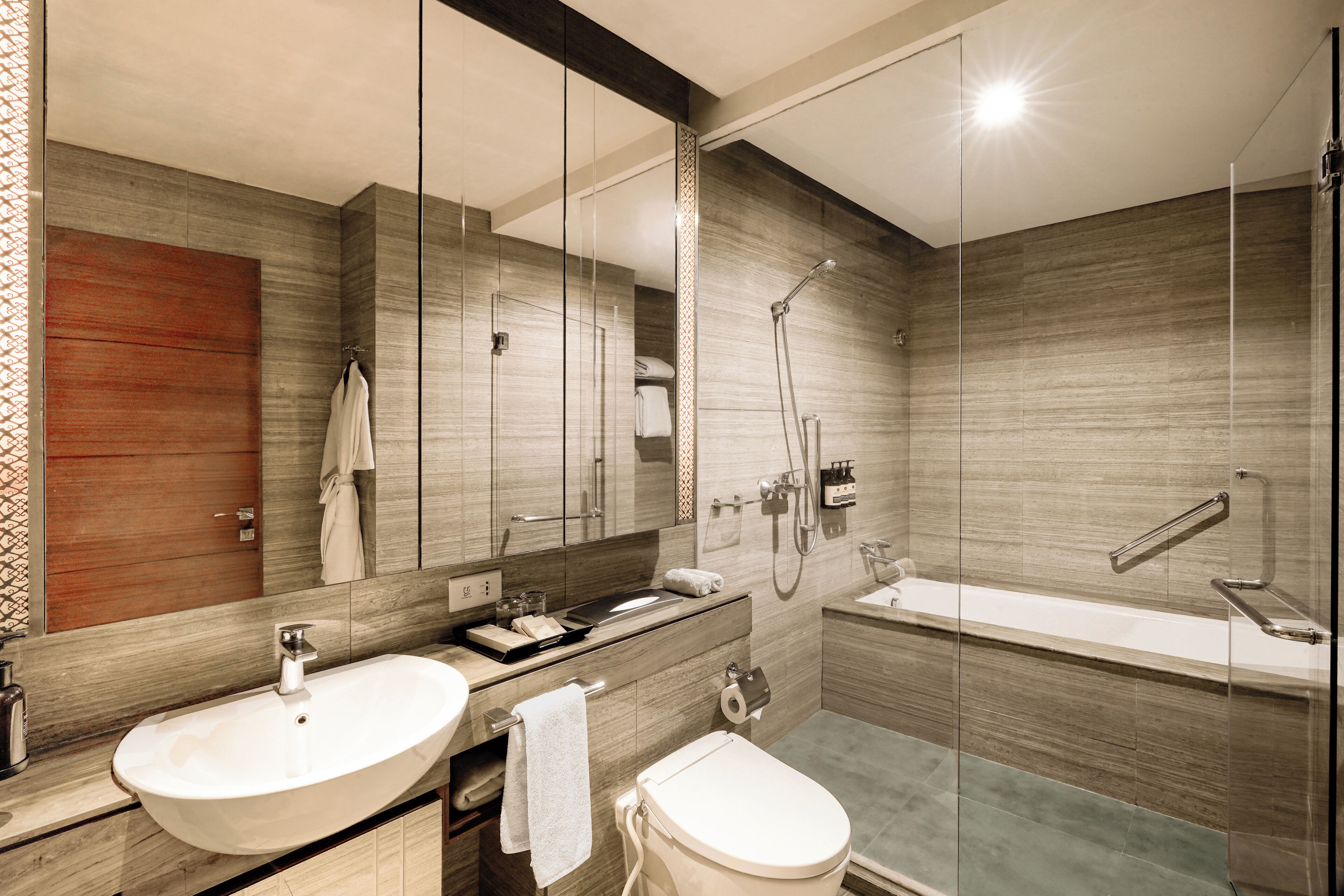 A modern bathroom with a large mirror, two sinks, a toilet, and a bathtub.