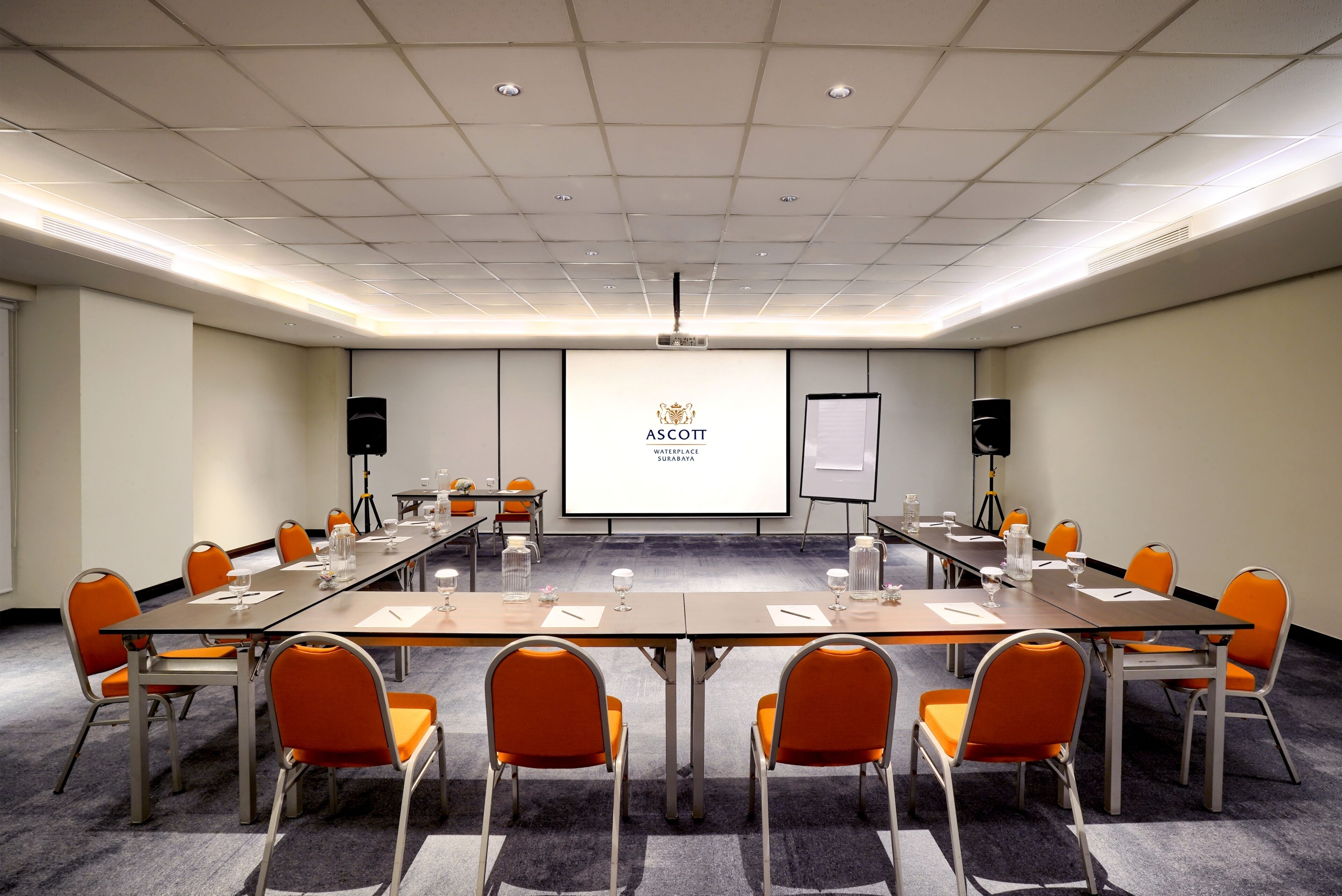 A conference room with a long table, orange chairs, a projector screen, and a whiteboard.