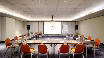 A conference room with a long table, orange chairs, a projector screen, and a whiteboard.