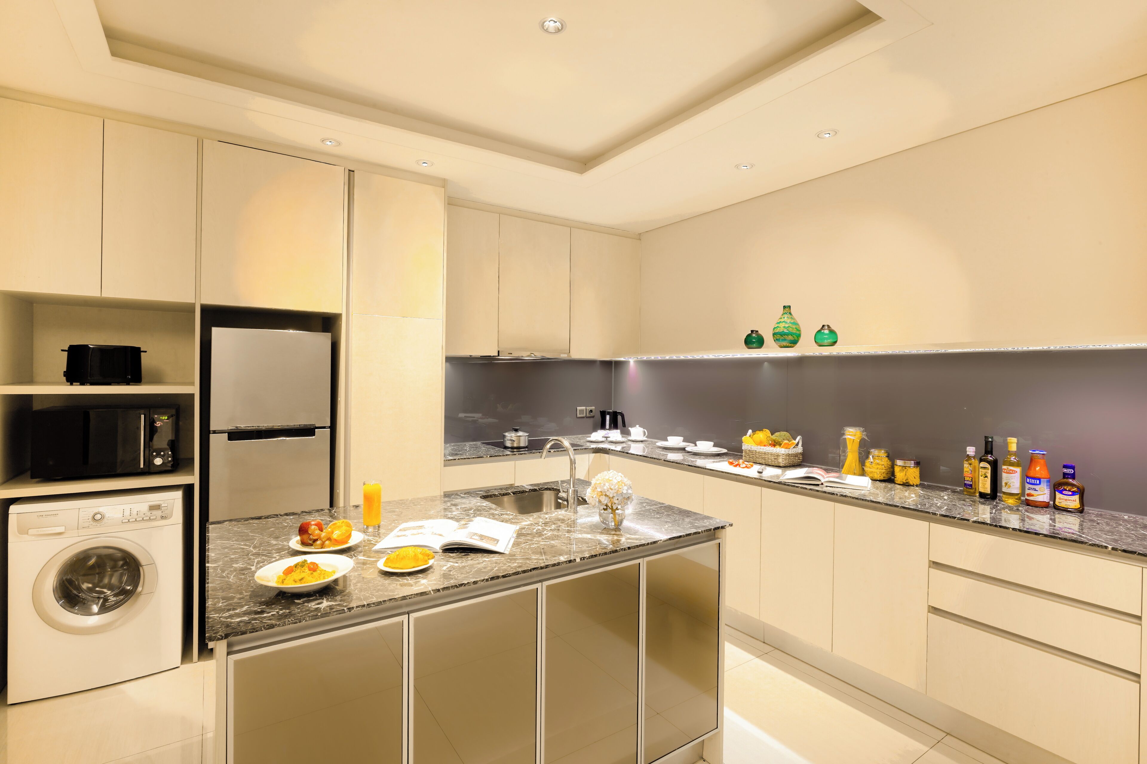 Una cucina moderna con lavatrice integrata, un piano di lavoro in granito e una varietà di elettrodomestici e utensili.