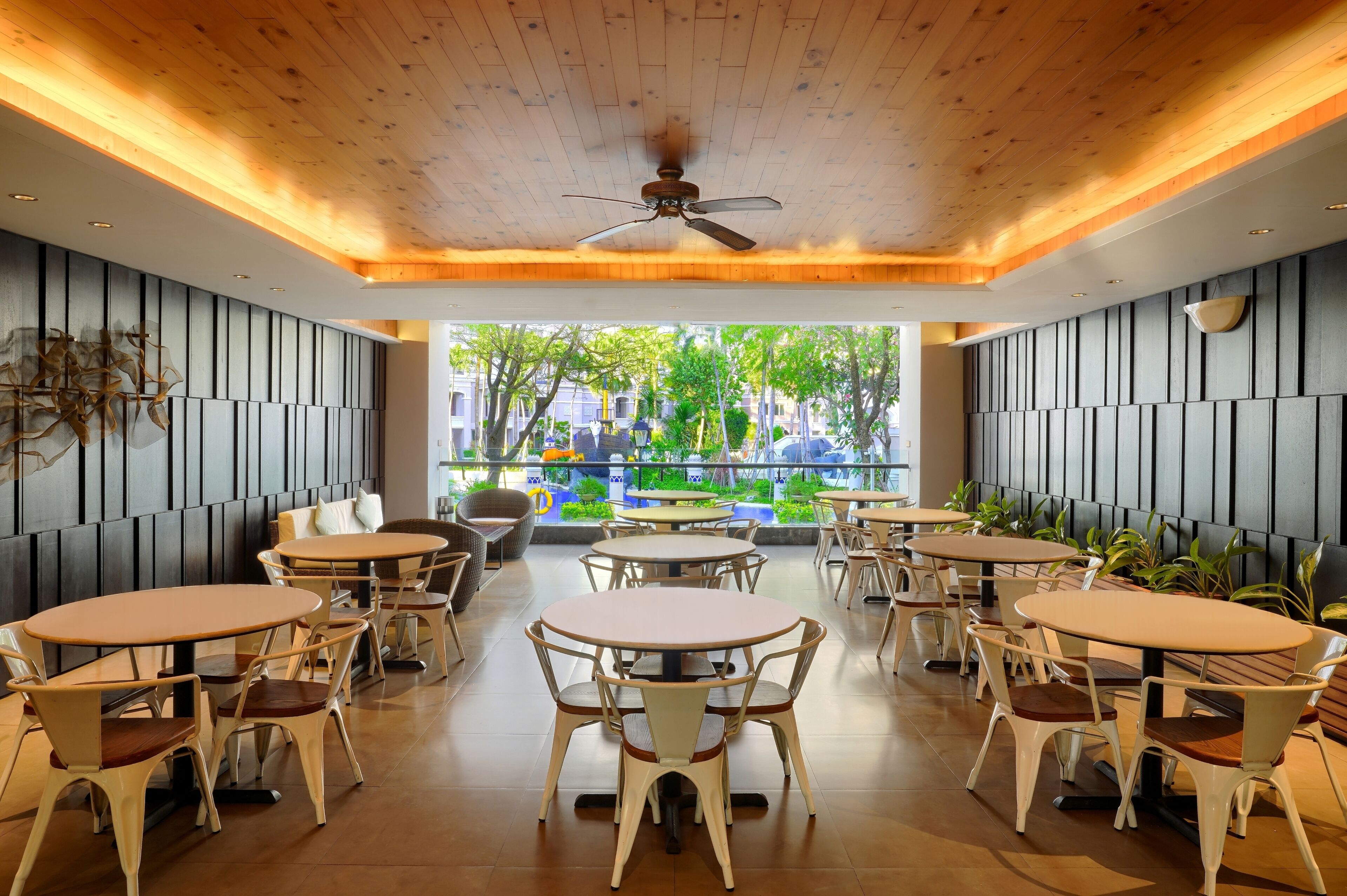 A modern indoor dining area with wooden ceiling, ceiling fan, and multiple round tables with chairs.