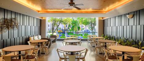 A modern indoor dining area with wooden ceiling, ceiling fan, and multiple round tables with chairs.