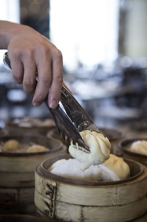 A hand using tongs to handle a food item in a bamboo steamer. - Pullman Taiyuan (Taiyuan)