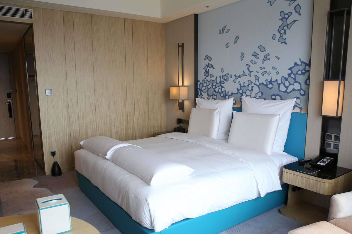 A hotel room with a large bed, bedside tables, a desk, and a wall with abstract art.