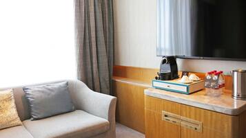 Een hotelkamer met een bank, een koffiezetapparaat, een televisie en een minibar.