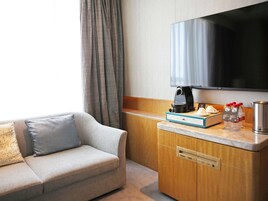 A hotel room with a sofa, a coffee maker, a television, and a minibar.