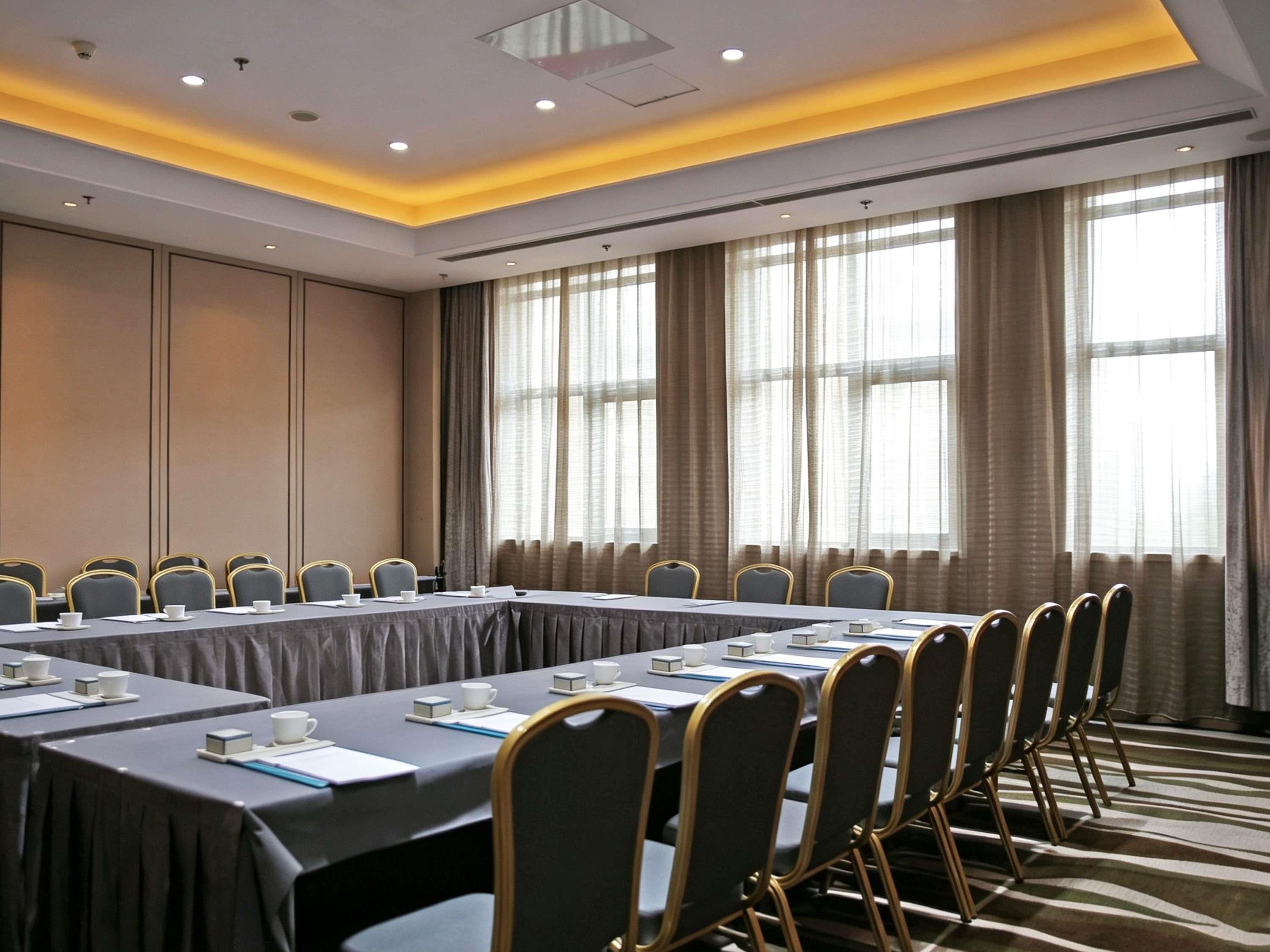A conference room with a long table, chairs, and a view of the outside through large windows.
