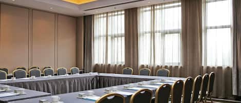 A conference room with a long table, chairs, and a view of the outside through large windows.