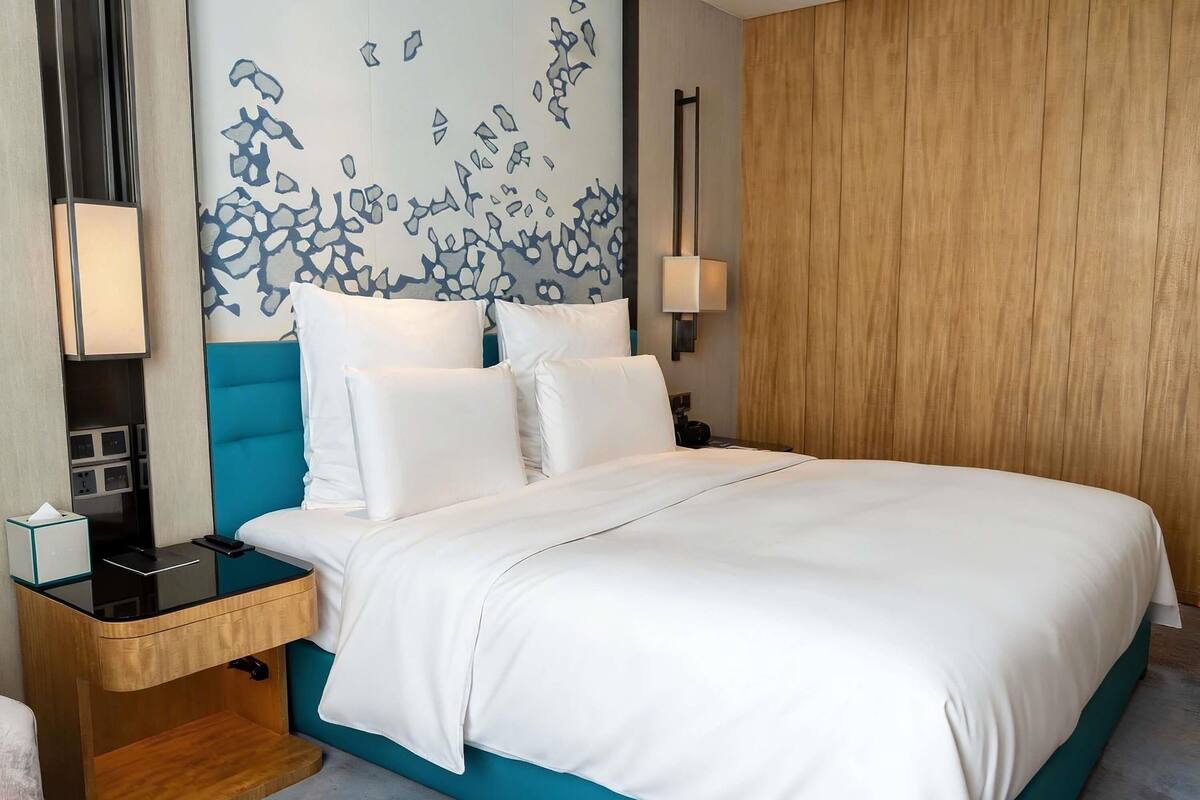 A hotel room with a bed, a nightstand, a lamp, and a wall with a blue abstract design.