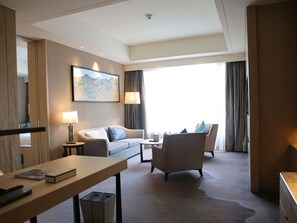 A hotel room with a sofa, armchair, and a small table with a lamp. There is a painting on the wall and a window with curtains. - Pullman Taiyuan (Taiyuan)