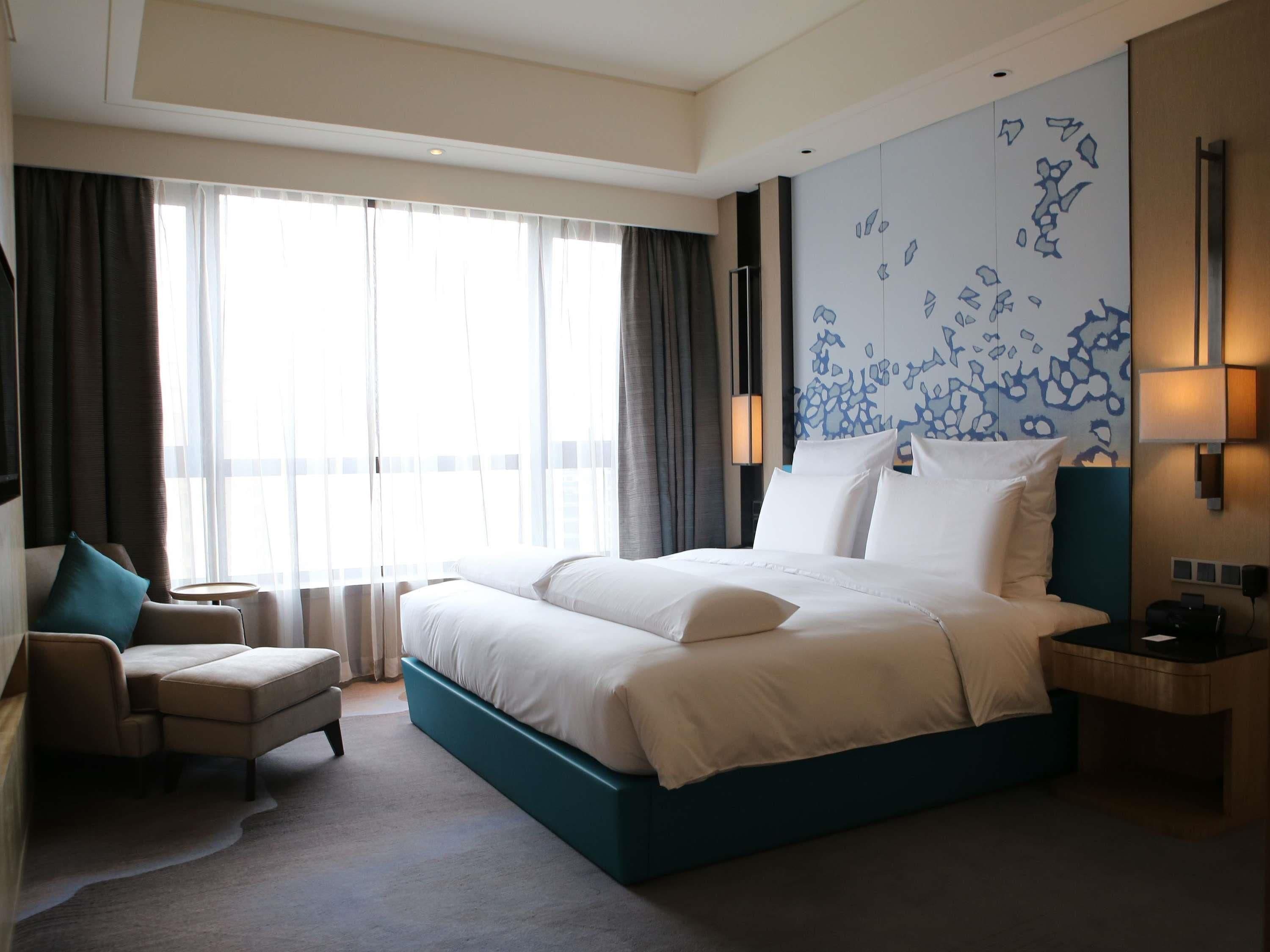 A hotel room with a large bed, a chair, a desk, and a view of the city.
