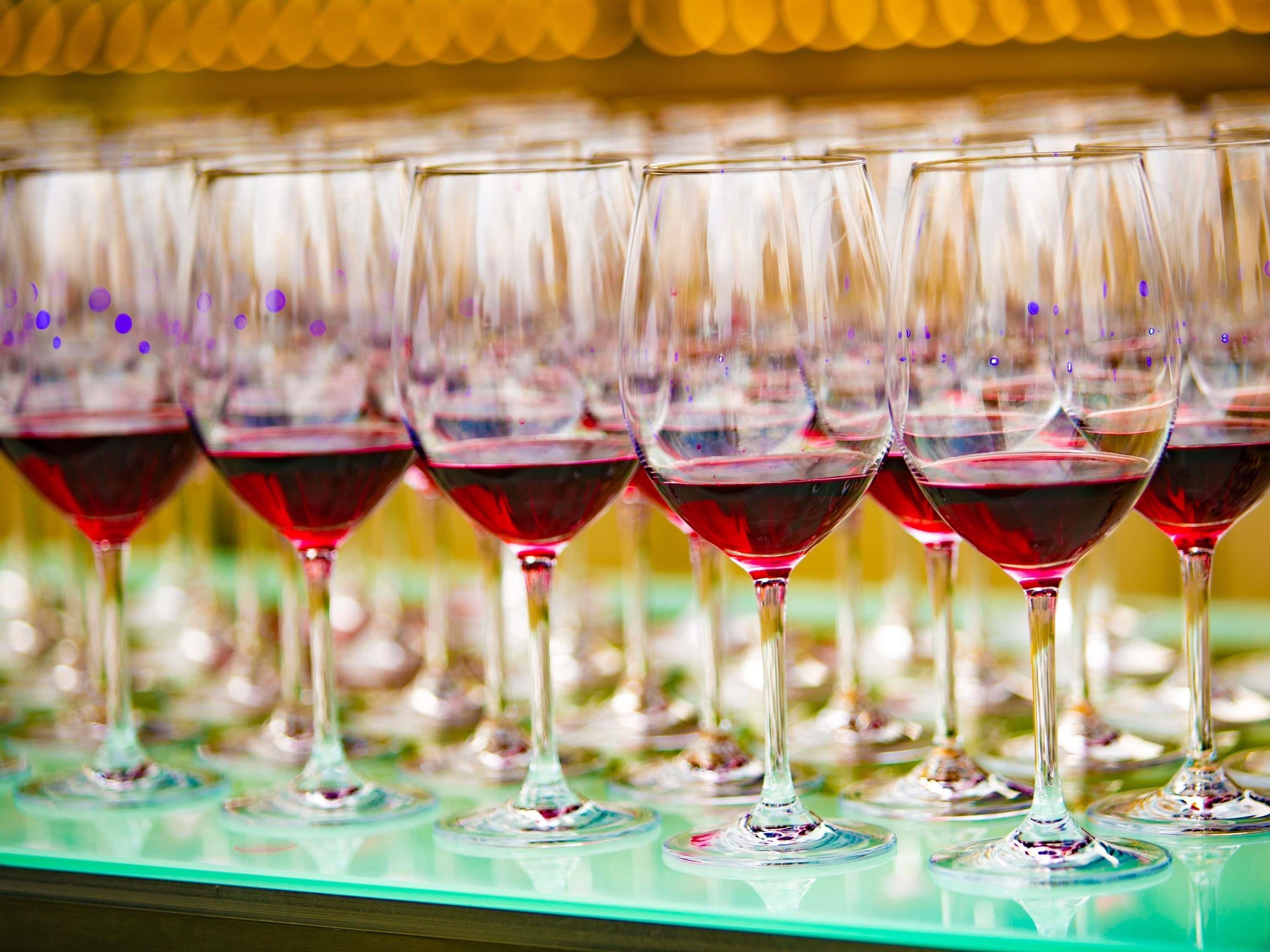 A row of wine glasses filled with red wine, placed on a reflective surface.