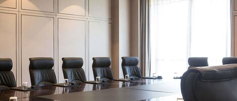 Un salón de conferencias con una larga mesa, varias sillas y un amplio ventanal con cortinas.