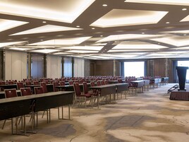 Un salón de conferencias con filas de mesas y sillas, un atril y ventanas amplias.