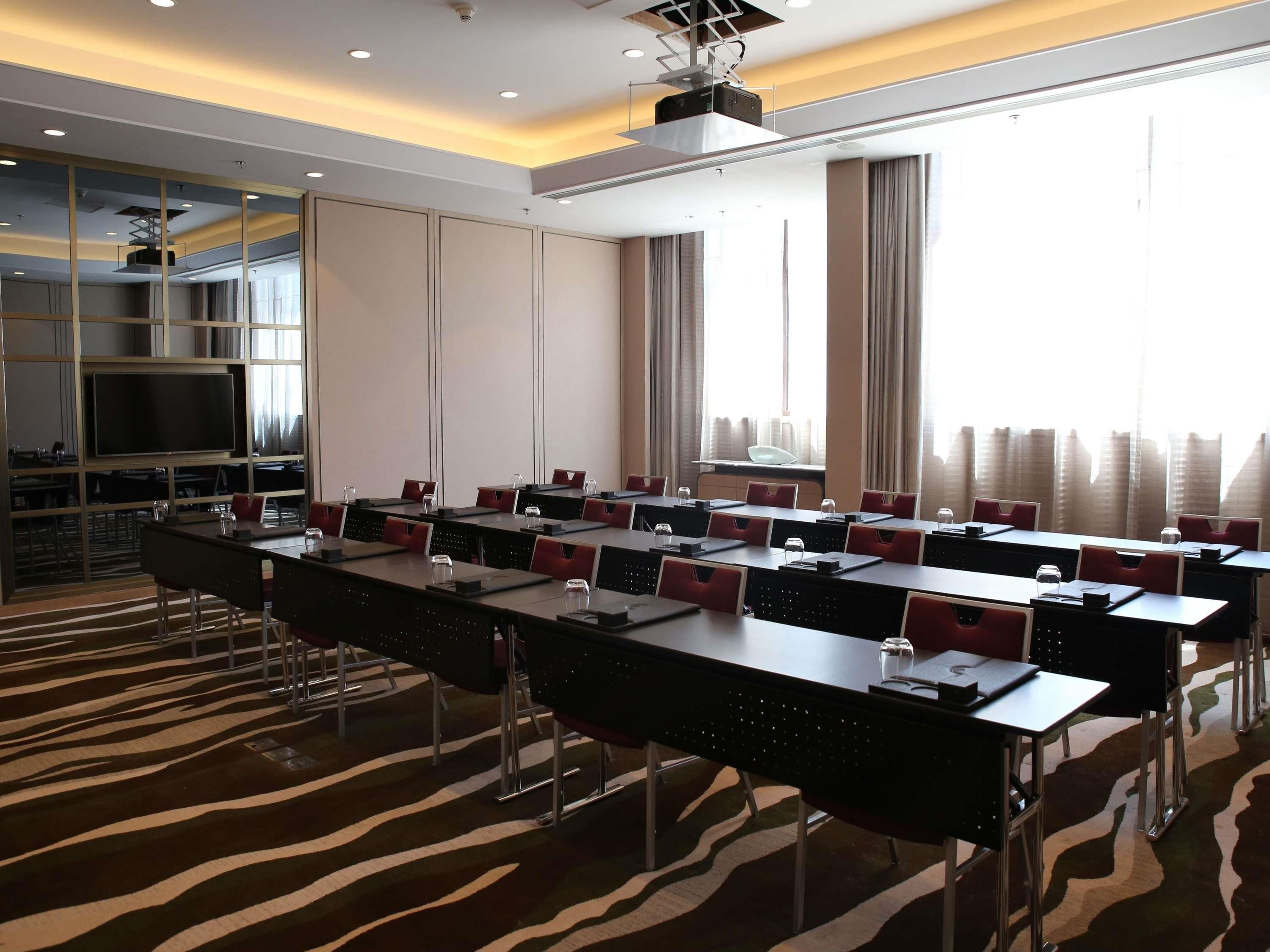 A conference room with long tables, chairs, a large screen, and a city view.