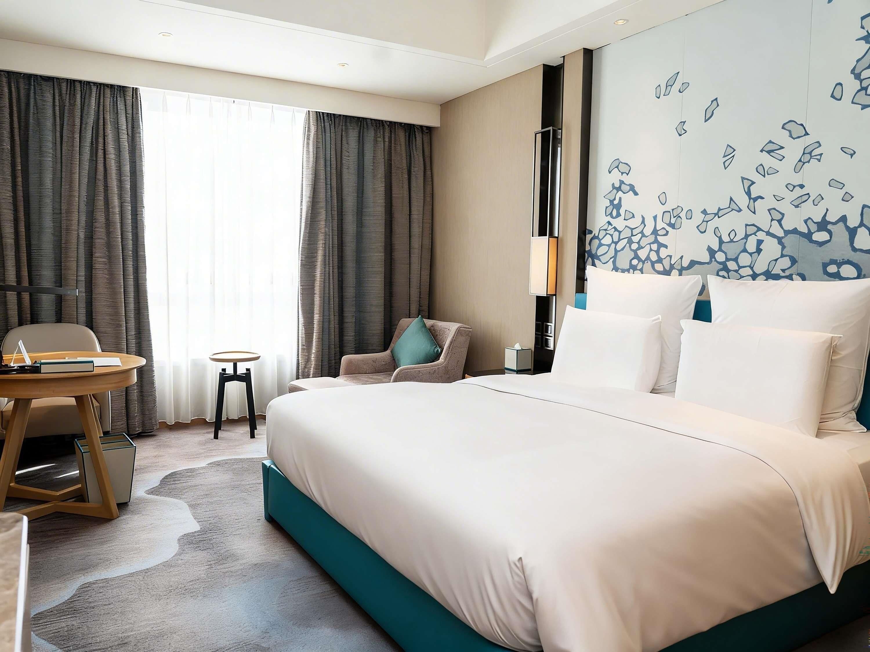 Habitación de hotel con una cama grande, un escritorio, una silla y una ventana con cortinas.