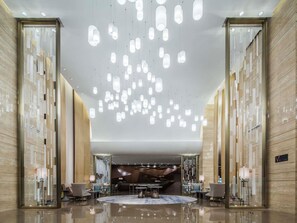 Eine großzügige Lobby mit hoher Decke, hängenden Pendelleuchten und einer zentralen Sitzecke.