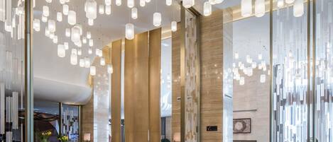 A modern lobby with hanging pendant lights, a reception desk, seating area, and a large glass wall.