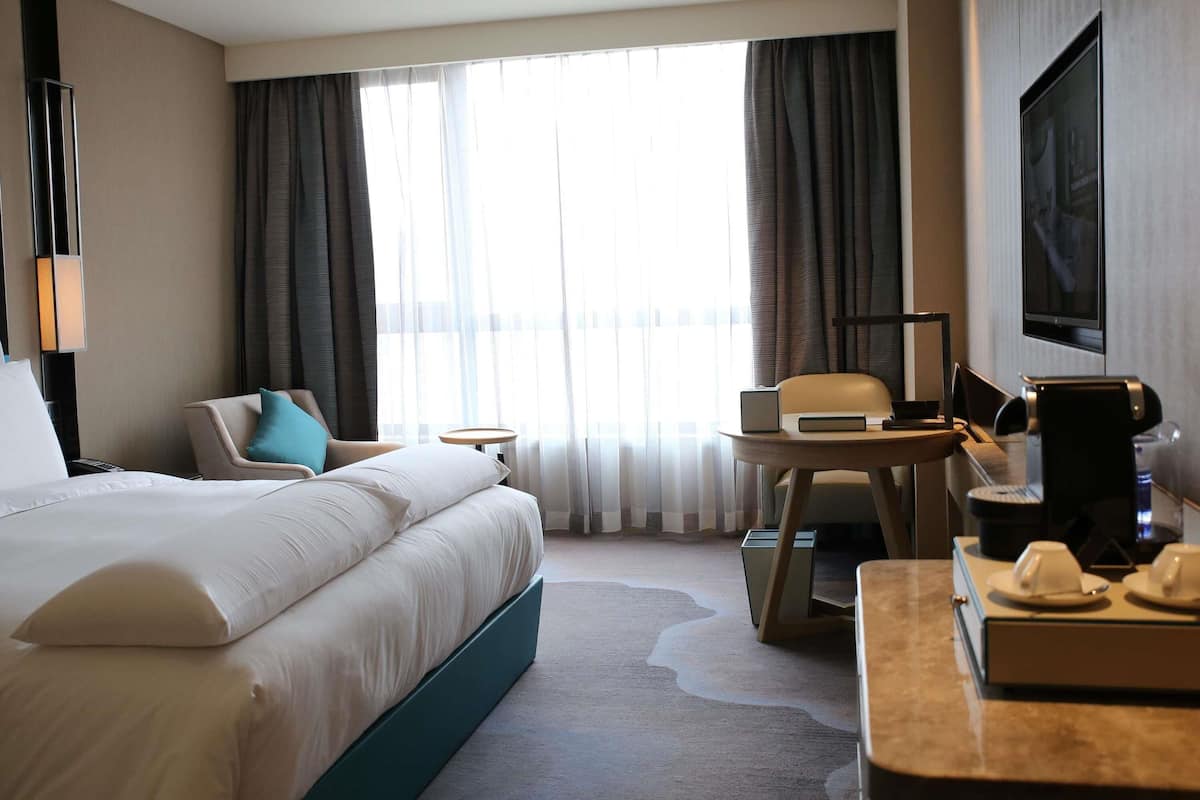 A hotel room with a large bed, a desk with a chair, a TV, and a window with curtains.