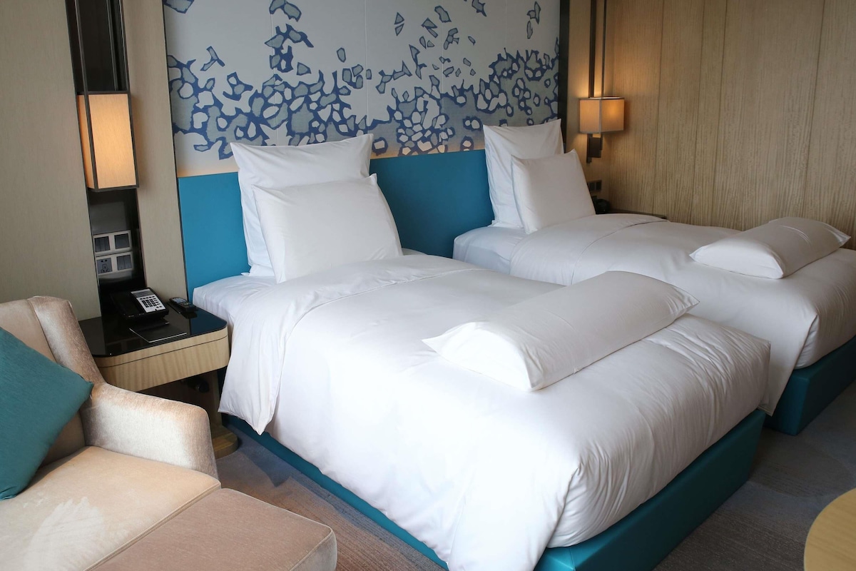 Habitación de hotel con una cama grande, una mesita de noche, una silla y una pared con un diseño abstracto azul.