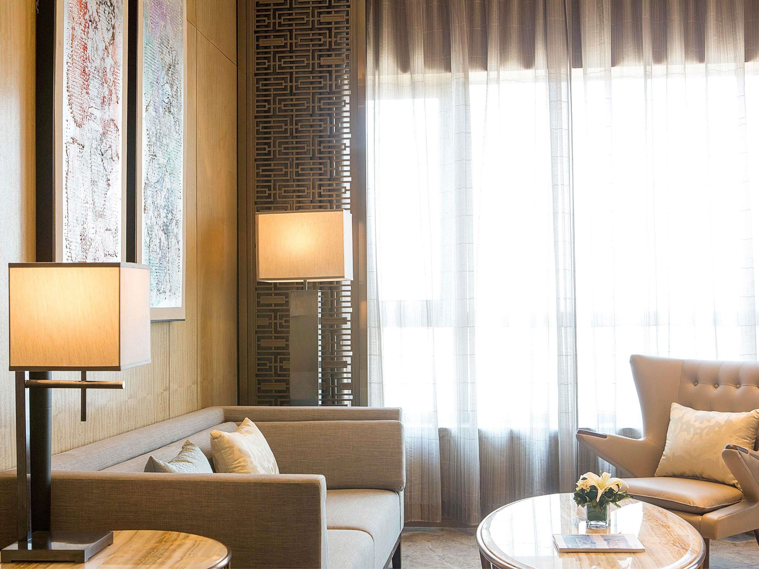 A hotel room with a sofa, armchair, round table, lamp, and decorative wall panels.