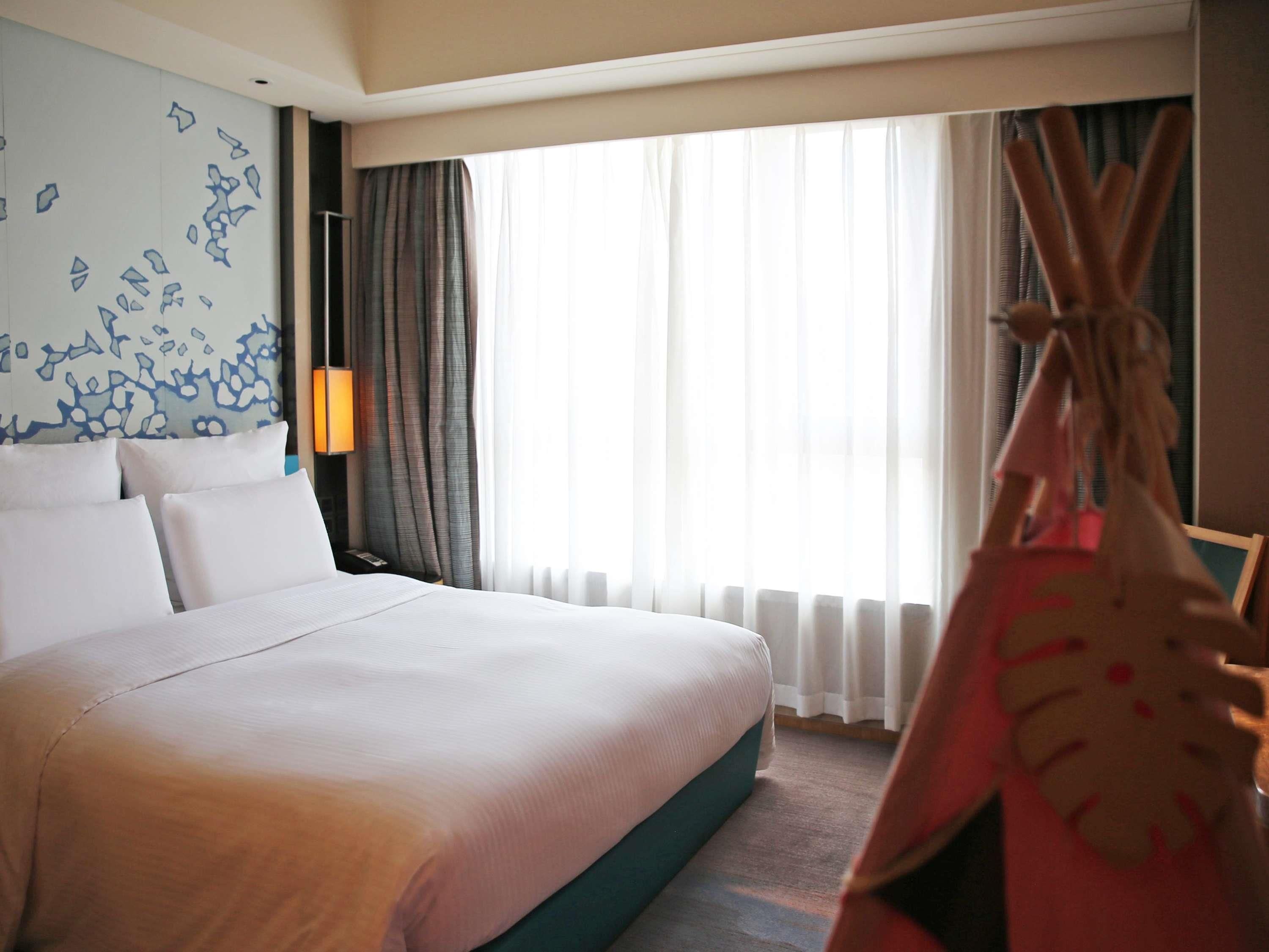 Ein Hotelzimmer mit einem großen Bett, einem Fenster mit Vorhängen, einer Wand mit abstrakter Kunst und einem dekorativen Gegenstand, der an ein Tipi erinnert.