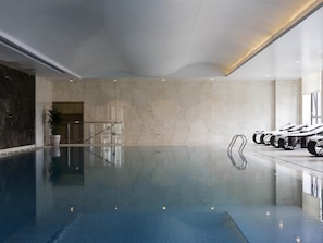 An indoor swimming pool with clear water, a marble wall, and a seating area with lounge chairs. - Pullman Taiyuan (Taiyuan)