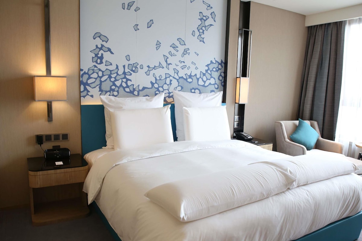 Habitación de hotel con una cama grande, un escritorio con teléfono, una silla y una pared con un diseño abstracto azul.