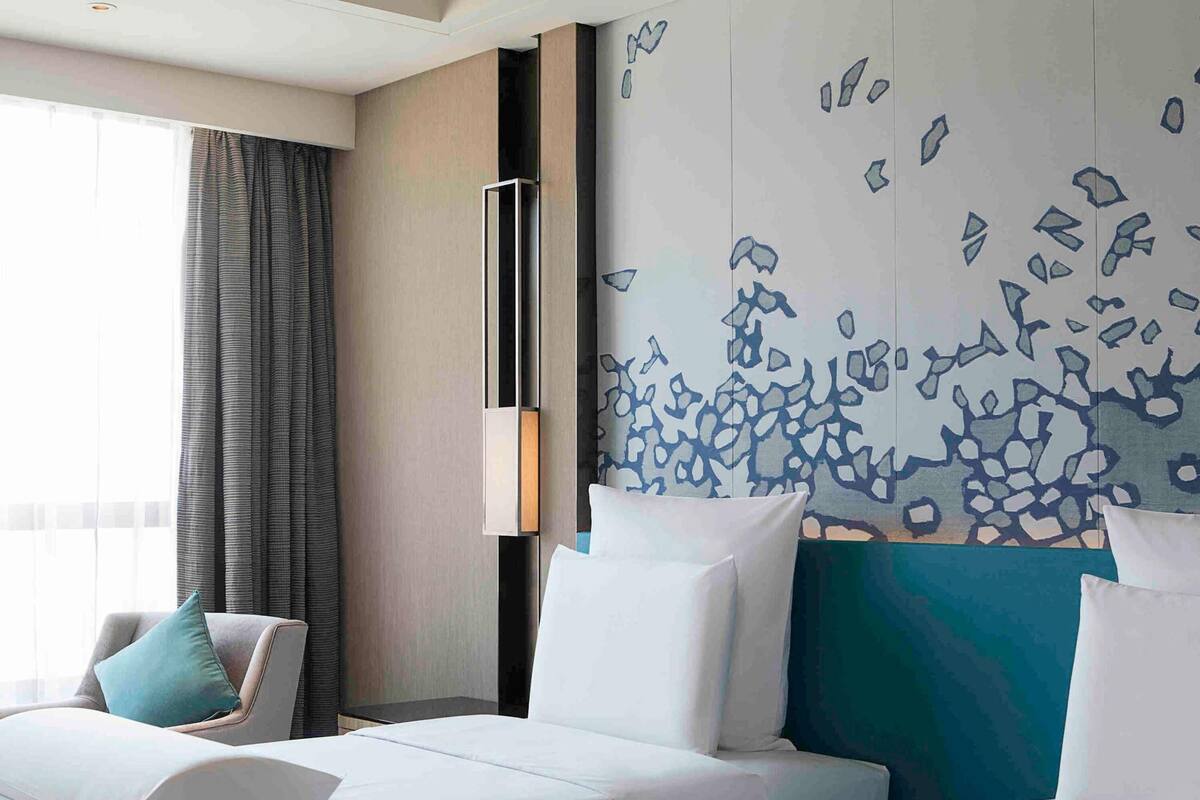 A hotel room with two beds, a large window with curtains, and a wall with abstract art.