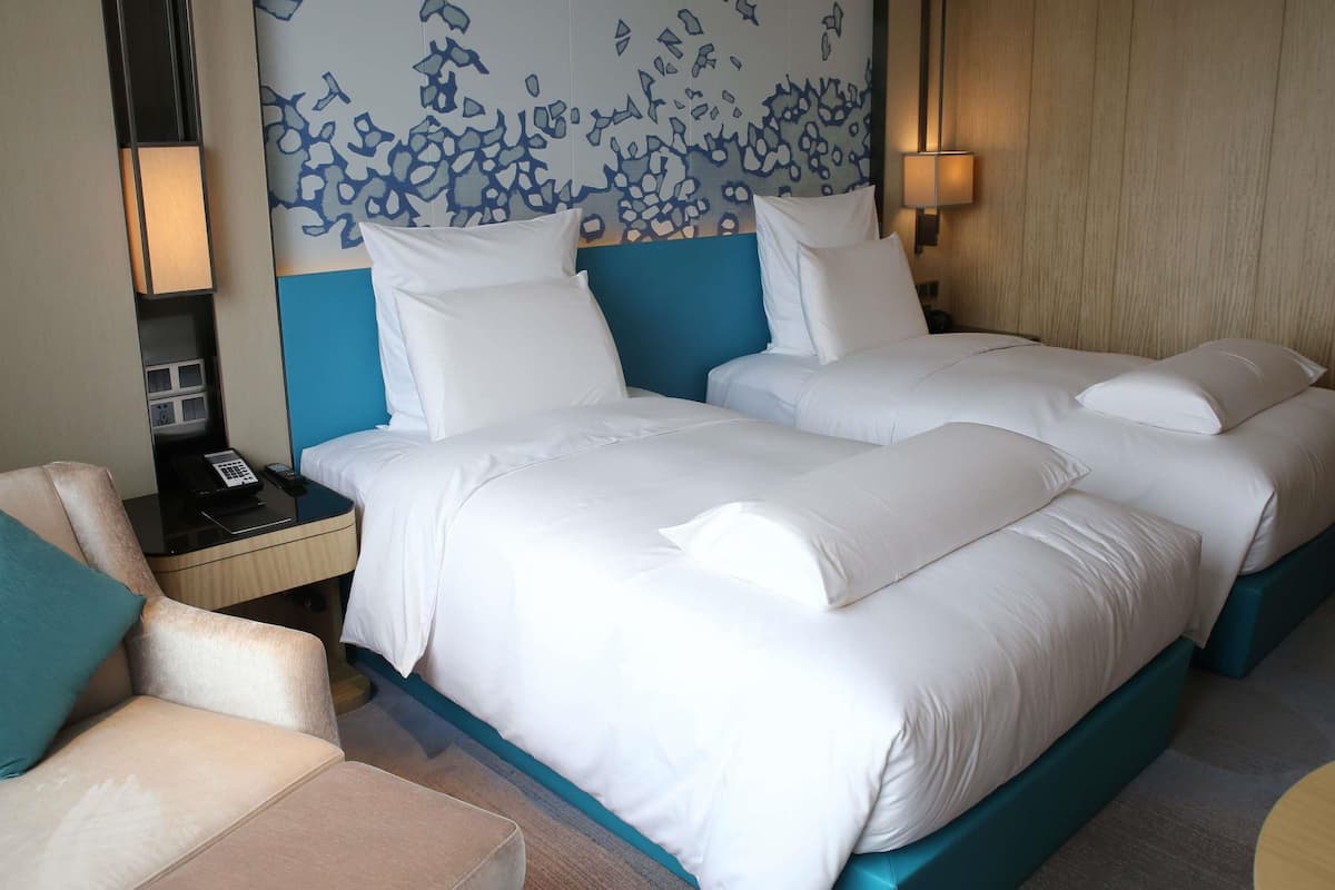 A hotel room with a large bed, a bedside table, a chair, and a wall with a blue abstract design.