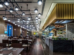 Un restaurante con varias mesas, iluminación colgante, una zona de cocina con ollas de cobre y una encimera de mármol.