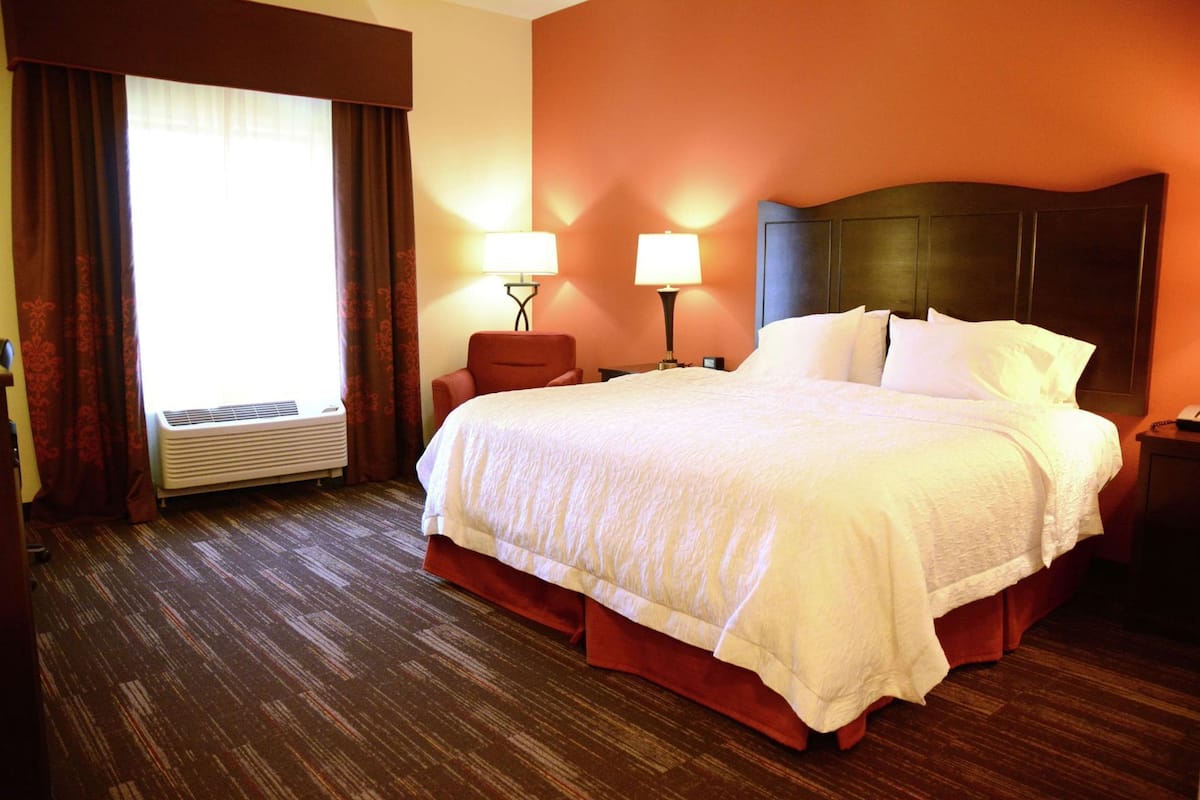 A hotel room with a large bed, two bedside lamps, a nightstand, and a window with curtains.