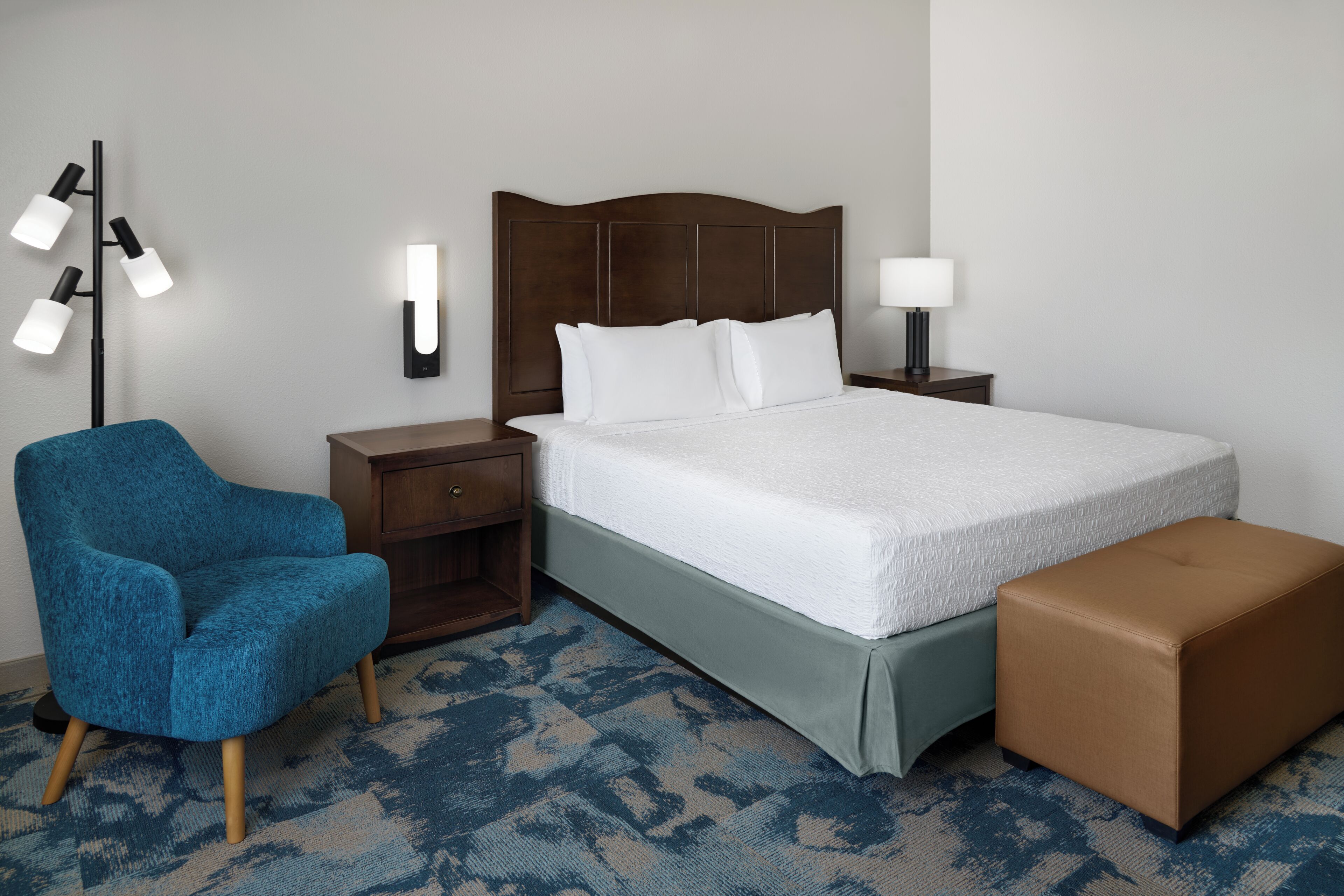 Une chambre d’hôtel comprenant un lit, une table de chevet avec une lampe, une chaise et une petite table.