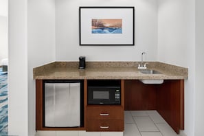 Una cocina compacta con microondas, cafetera, lavamanos y un refrigerador pequeño.