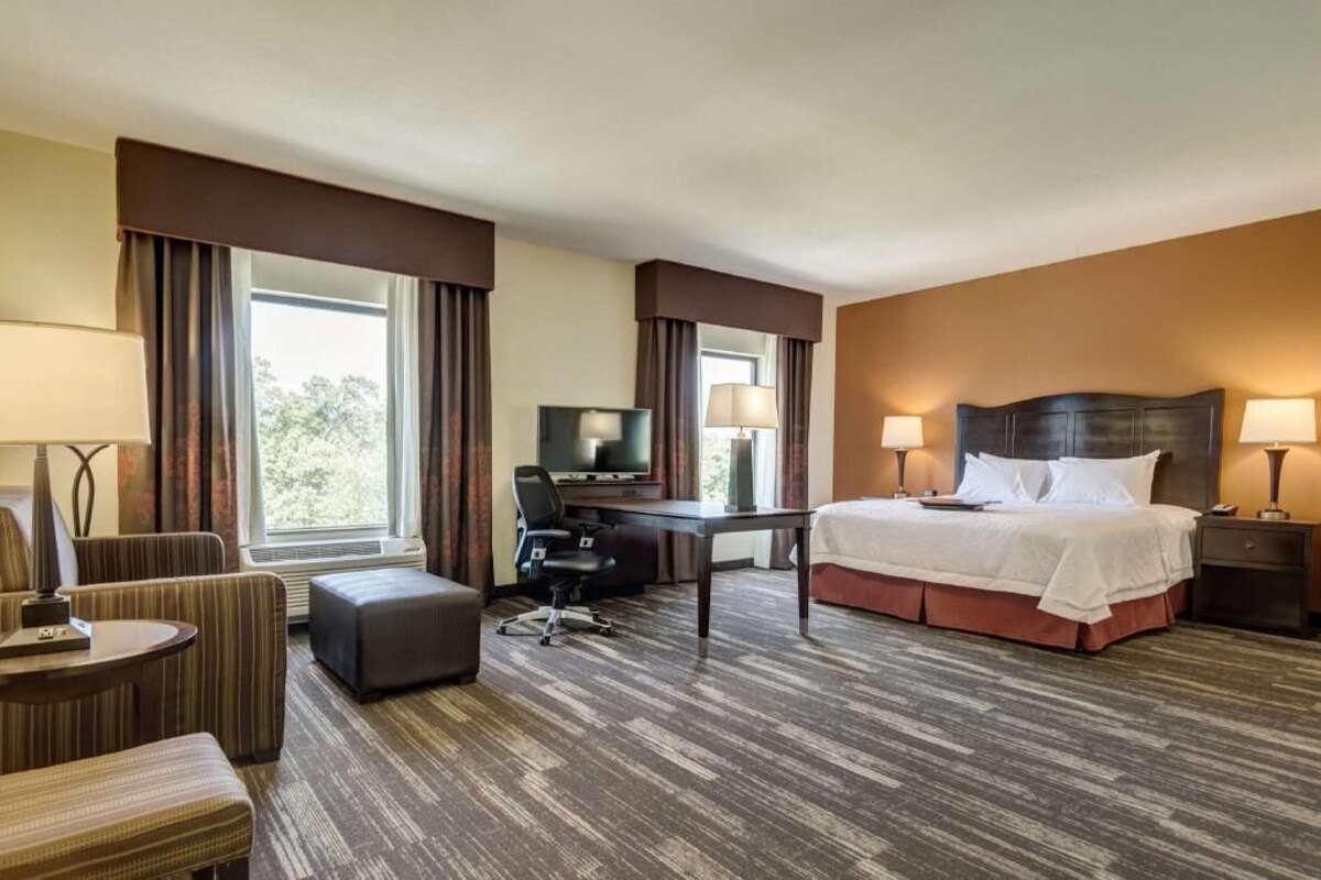 Habitación de hotel con cama, escritorio, silla, televisor y ventanas.