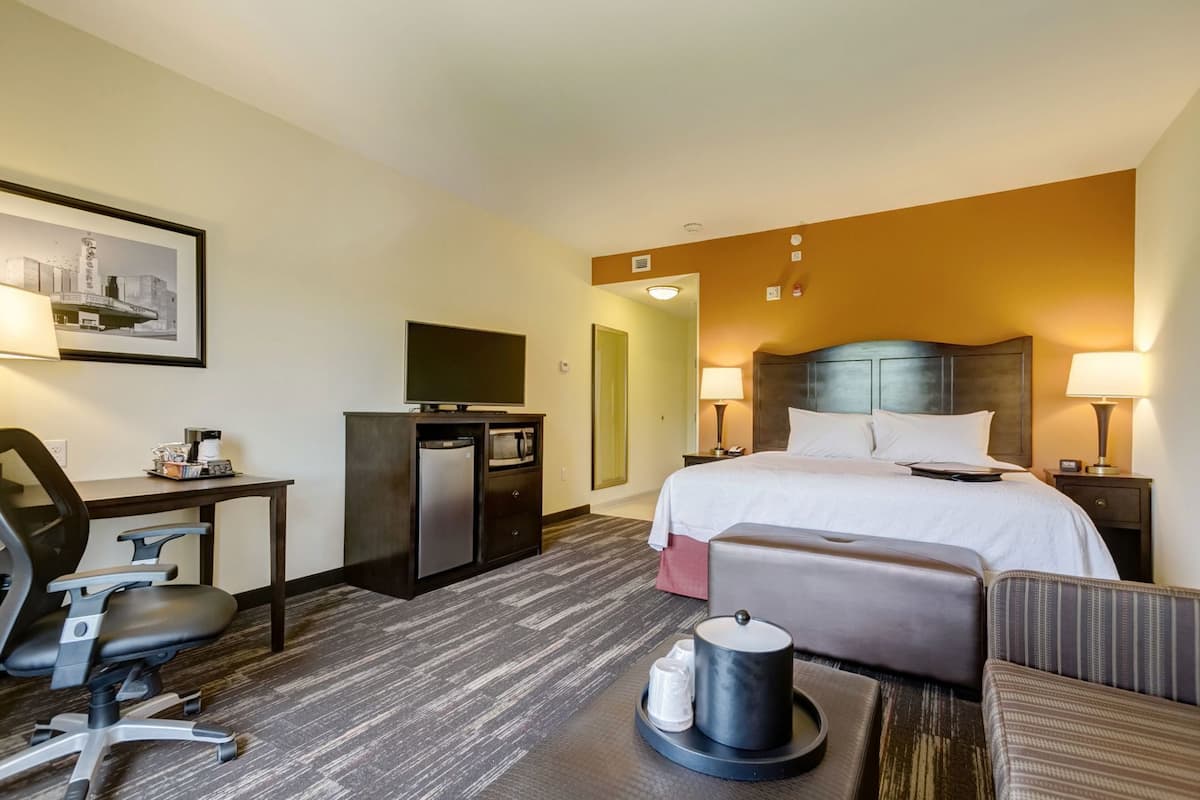 A hotel room with a bed, desk, chair, TV, and a small refrigerator.