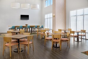 A spacious dining area with multiple tables and chairs, a flat-screen TV mounted on the wall, and large windows providing natural light. - Hampton Inn Poplar Bluff (Poplar Bluff)