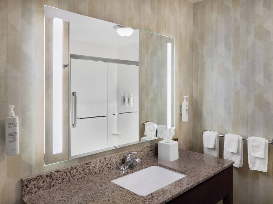 A bathroom with a granite countertop, a white sink, a large mirror, and a towel rack.