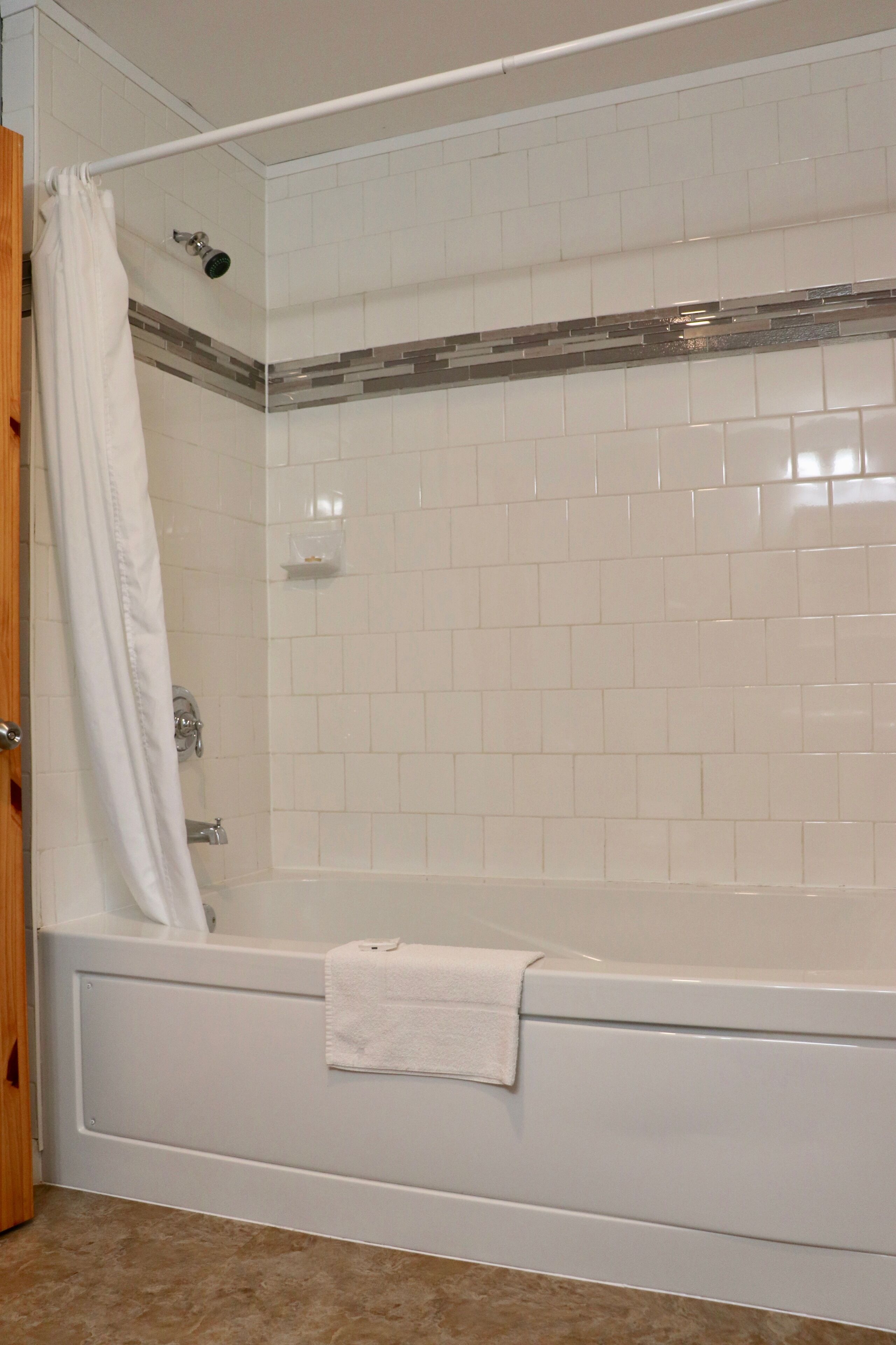A bathroom with a white bathtub, a shower, and a tiled wall.