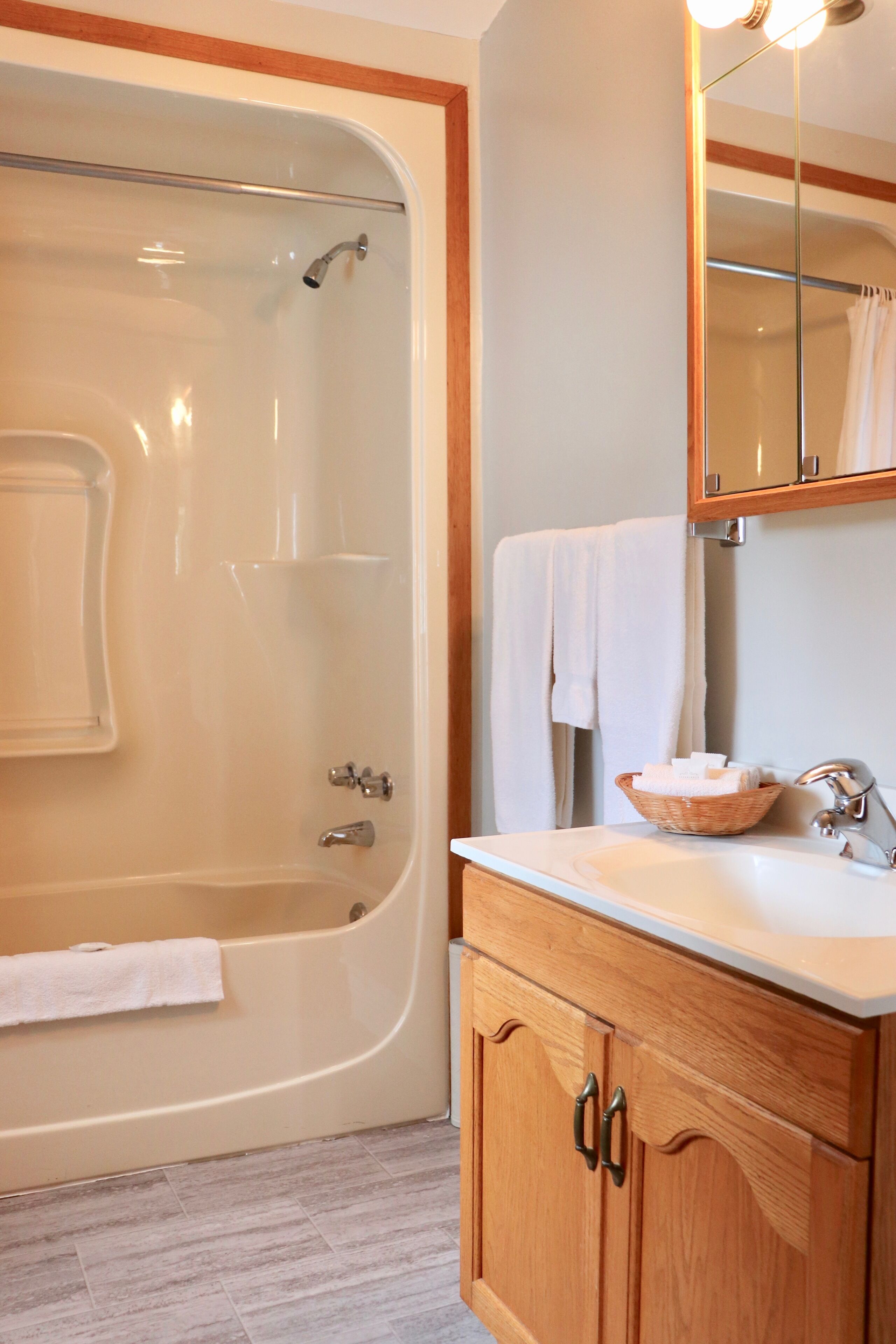 A bathroom with a bathtub, a sink, a mirror, and wooden cabinets.