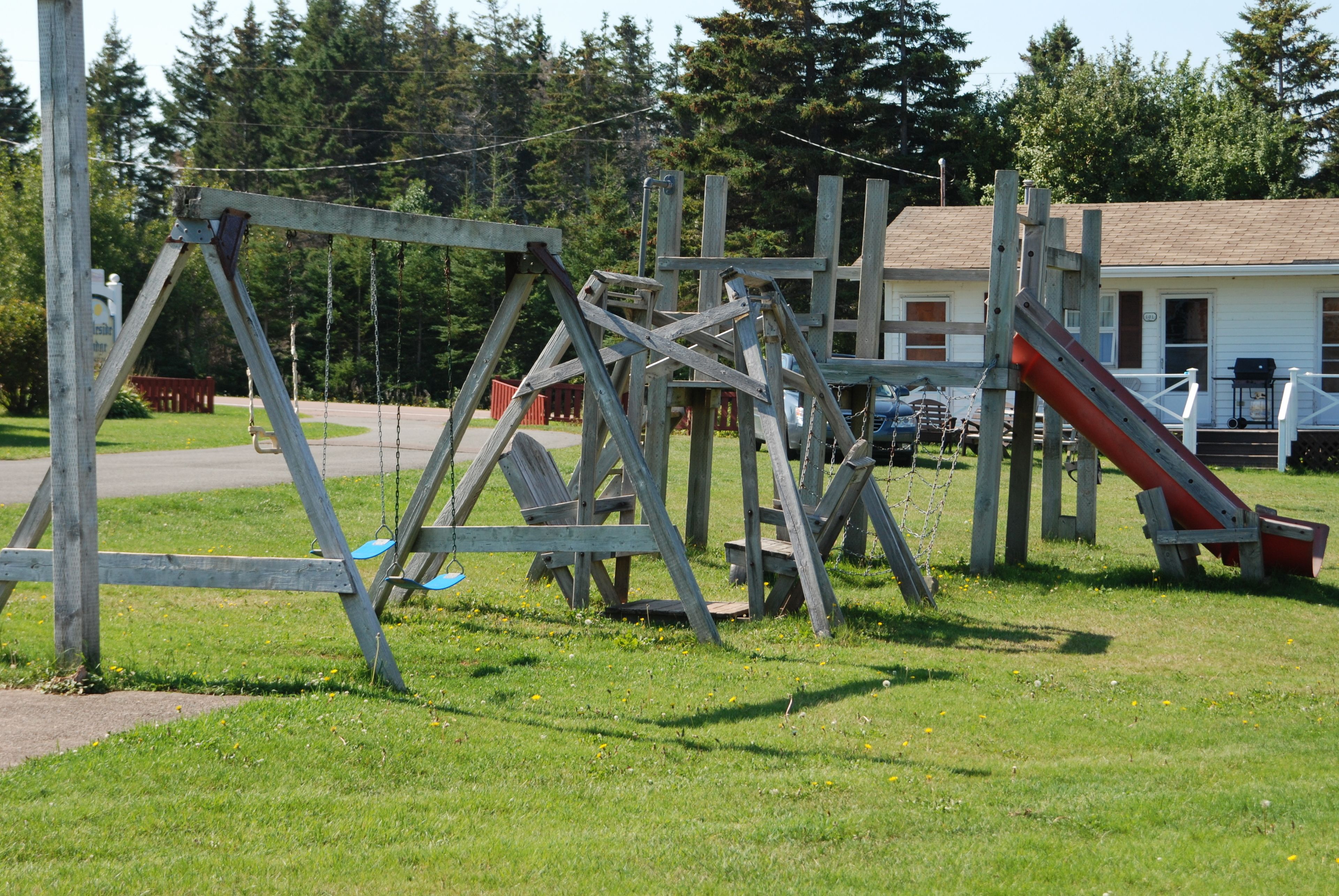 A playground with swings and a slide, surrounded by a grassy area and trees.