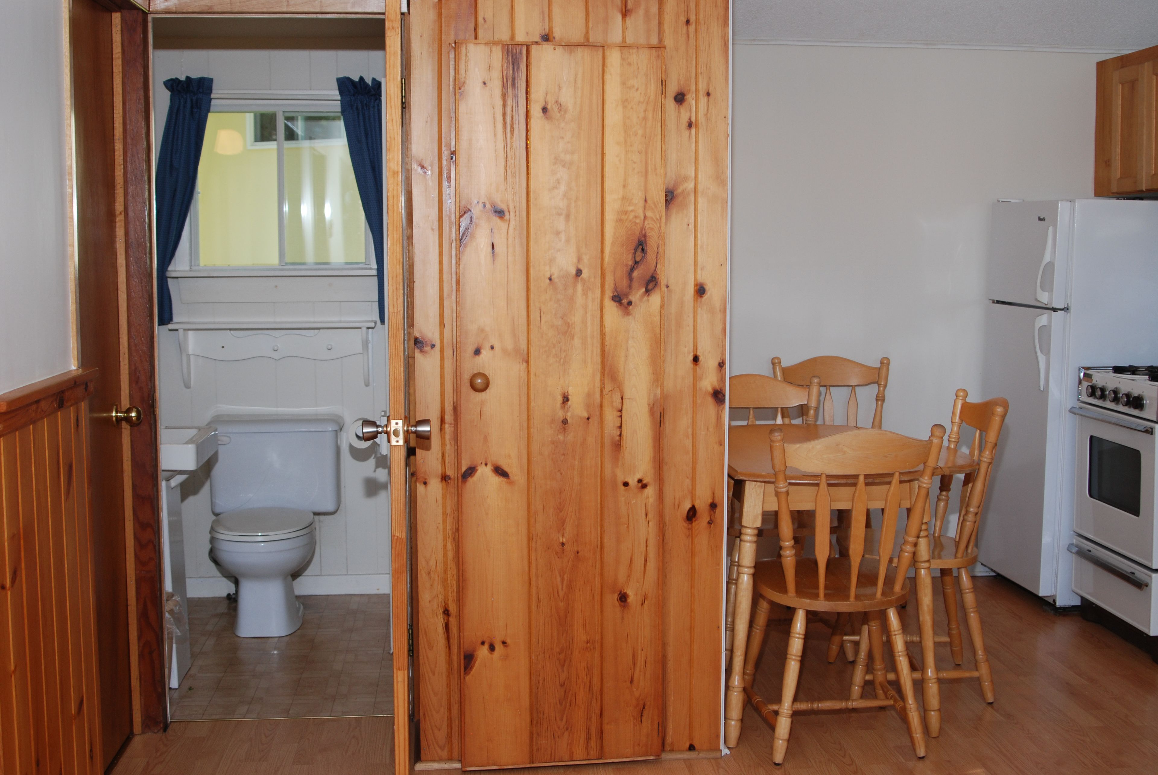 A wooden door leading to a bathroom with a toilet and a window with curtains.